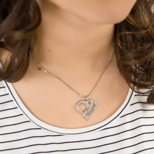 Collier orné d'un pendentif qui représente deux coeurs entrelacés, gravés avec deux prénoms, porté par une femme